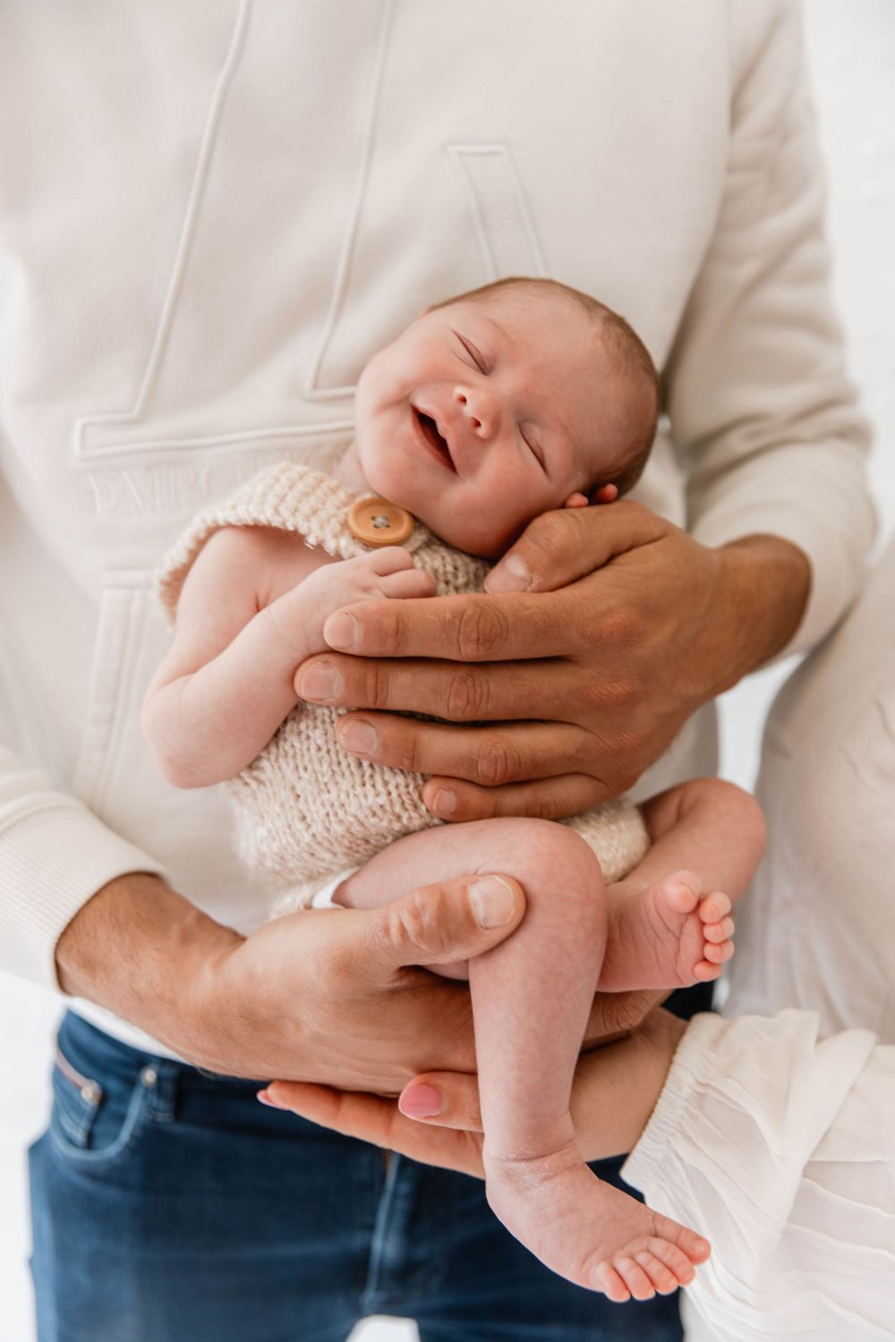 Tender montage sequence shows adult hands gently cradling and holding a sleeping newborn baby in white clothing.