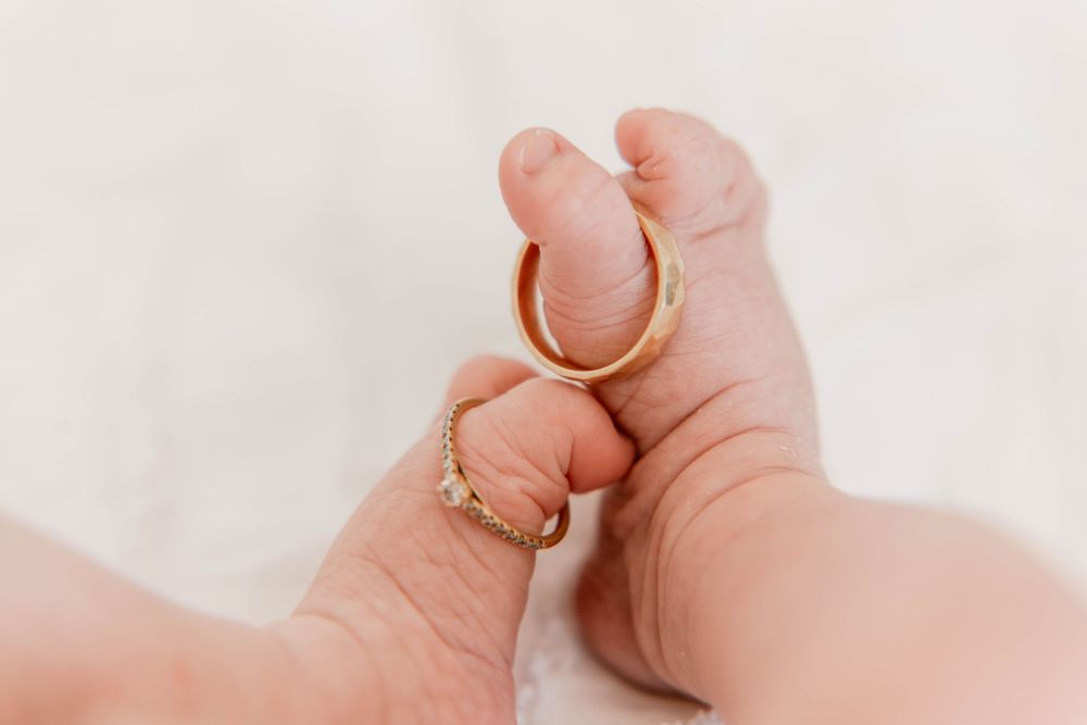 Two gold wedding rings displayed on tiny baby feet against a white background.