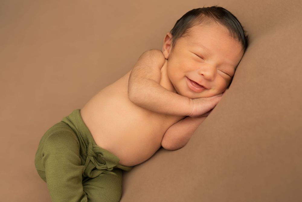 Peaceful newborn in green pants sleeping on brown background.