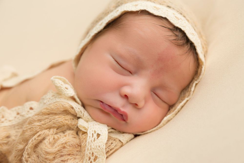 Sleeping newborn wearing cream bonnet on beige background.