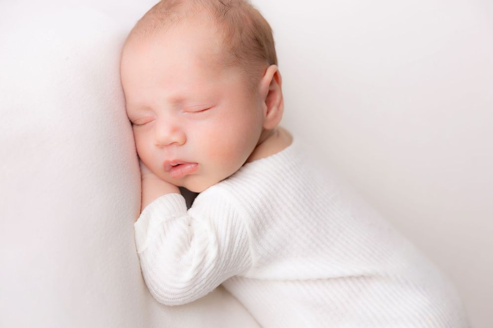 A sleeping baby wrapped in white swaddling blankets rests peacefully against a light background.