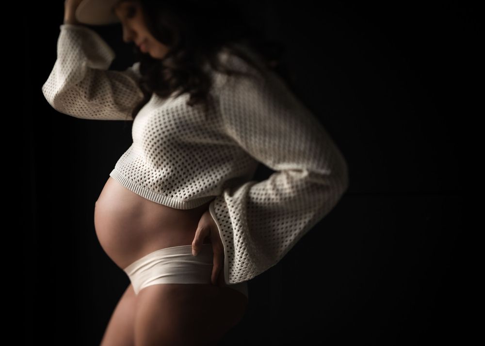Artistic maternity photoshoot silhouettes showing a pregnant figure in various poses against a dark background.