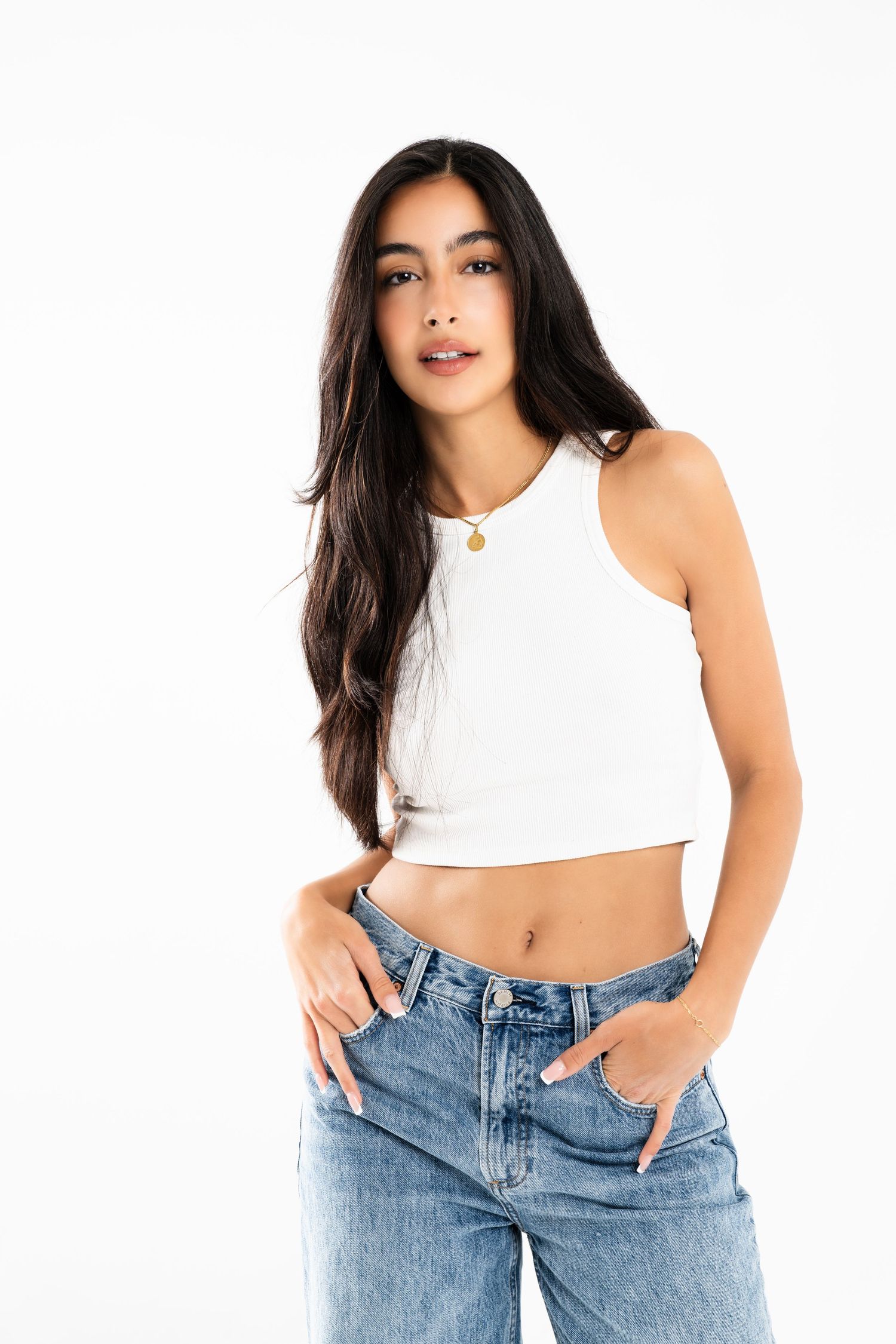 Fashion model in white crop top and light wash denim jeans against white background.