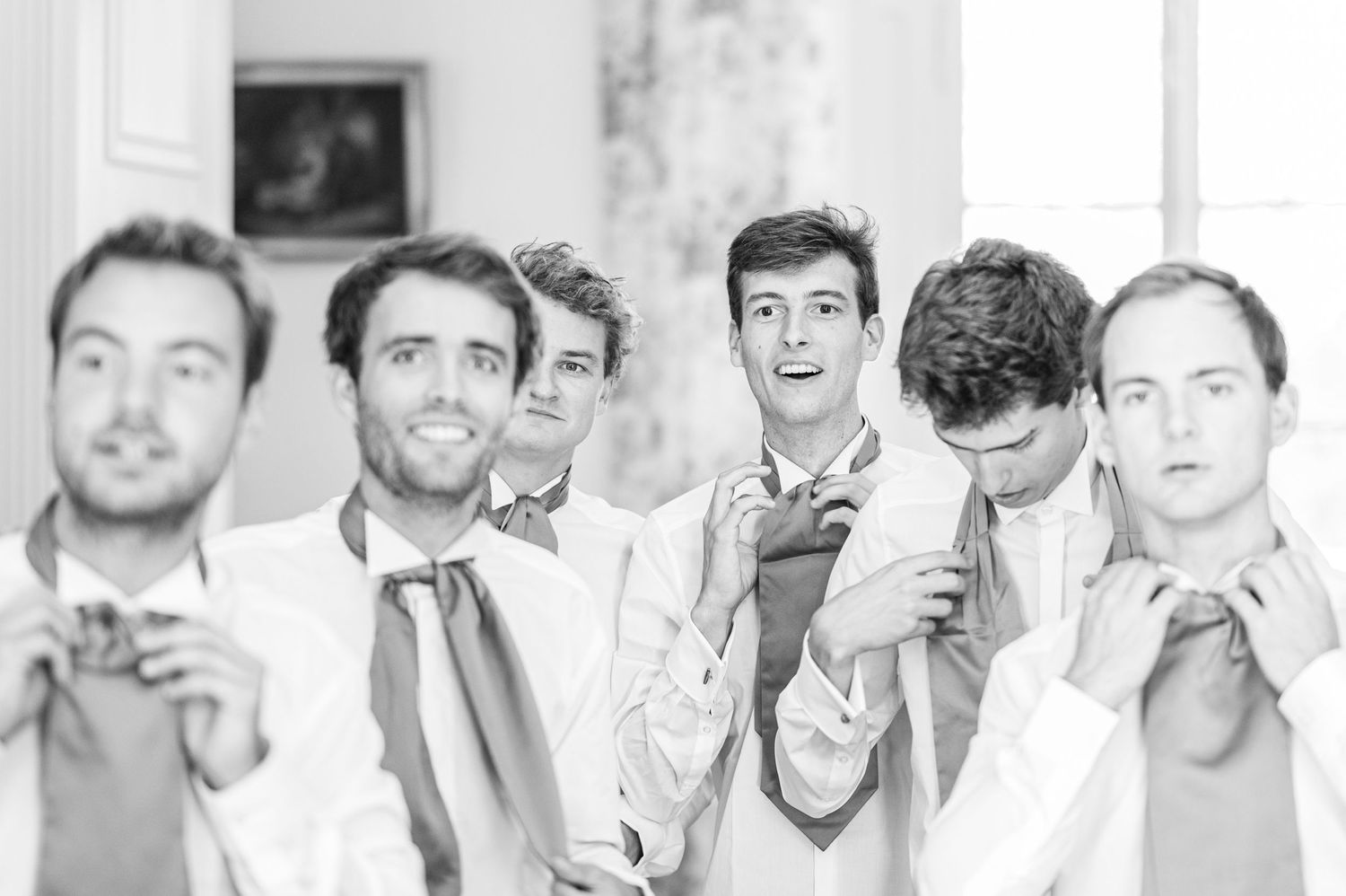 Black and white photo of groomsmen adjusting their ties while getting ready.
