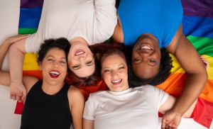 Friends laughing together while lying on rainbow pride flag with glitter.