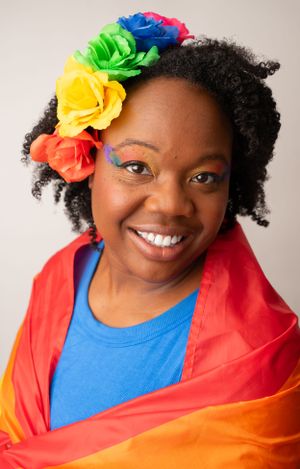 Person with rainbow flower accessory and colorful makeup smiling brightly.
