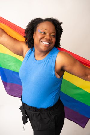 Joyful pose with rainbow pride flag spread wide against white studio background.