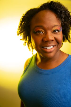 Colorful portrait with purple eye makeup against warm yellow background.