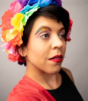 Colorful flower crown and red lipstick create a vibrant portrait against gray background.