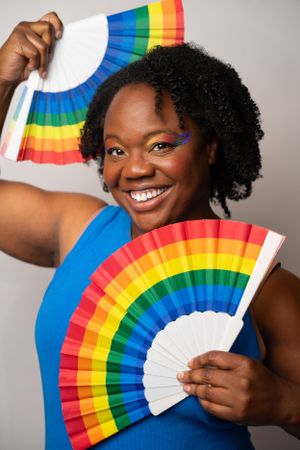 Person in blue top holding rainbow folding fan with joyful expression.