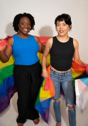 Friends standing together while holding up a colorful pride flag in a studio setting.