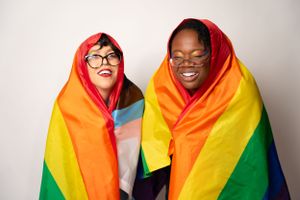 Two people wrapped in colorful pride flag smiling and posing together.