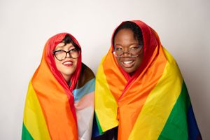 Friends sharing intimate moment while draped in rainbow pride flag.