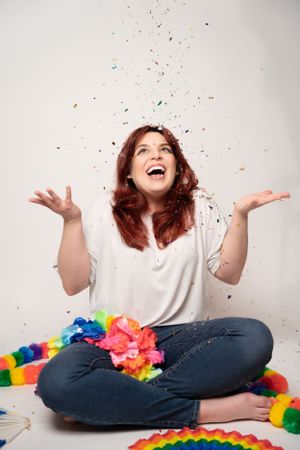Celebratory pose with arms raised surrounded by rainbow decor and floating confetti.