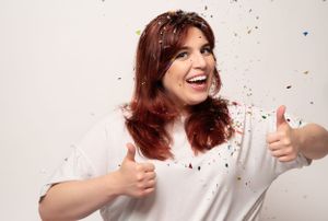Person with auburn hair joyfully expressing themselves against a white background with colorful confetti.