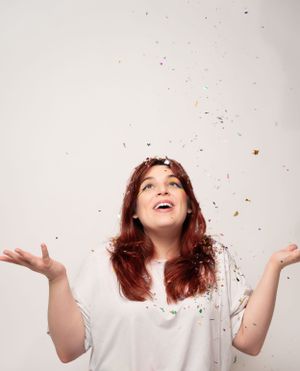 Person in white shirt gesturing with hands while confetti falls in a bright studio setting.