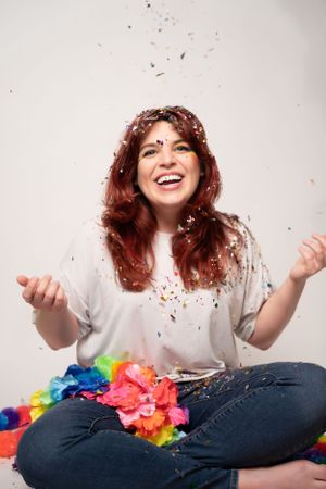 Person in white shirt and jeans sitting while colorful confetti rains down in studio.