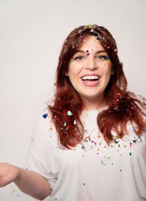 Person with wavy hair spreading arms while confetti creates a festive atmosphere.