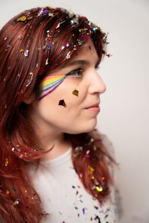 Side profile with rainbow makeup and shimmering confetti against white backdrop.