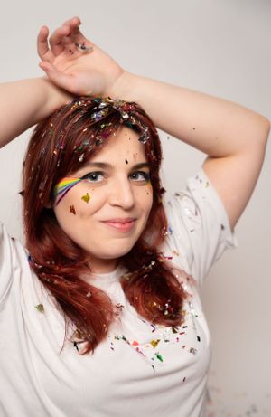 Casual pose in white t-shirt with rainbow accents and falling confetti.