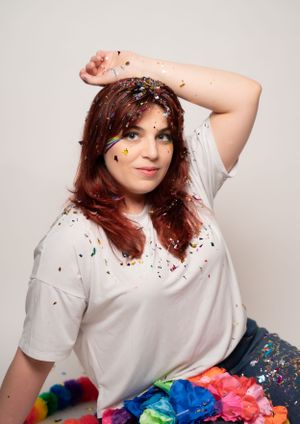 Creative portrait with colorful rainbow props and scattered glitter against white backdrop.