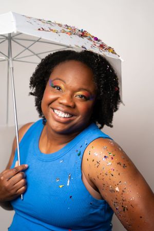 Bright studio portrait with white umbrella and scattered rainbow glitter effects.