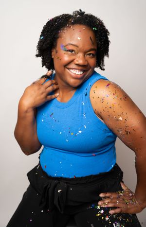 Dynamic studio pose with blue top and scattered confetti creating movement.