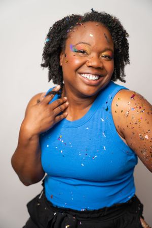 Portrait against white background wearing bright blue tank top with glitter makeup and natural curls.