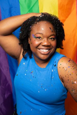 Expressive poses against vibrant rainbow background with sparkly makeup and blue sleeveless top.