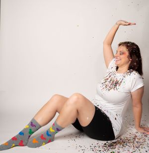 Dynamic floor poses in white shirt and patterned socks with colorful confetti scattered around.