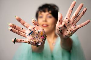 Hands covered in colorful glitter shown against mint green tulle dress background.