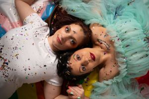 People lying on ground covered in rainbow glitter and mint green tulle fabric.