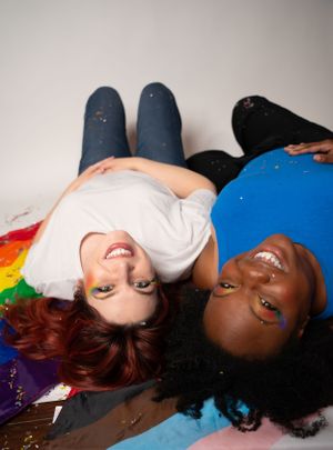 Friends lying on rainbow flag smiling with glitter scattered around them.
