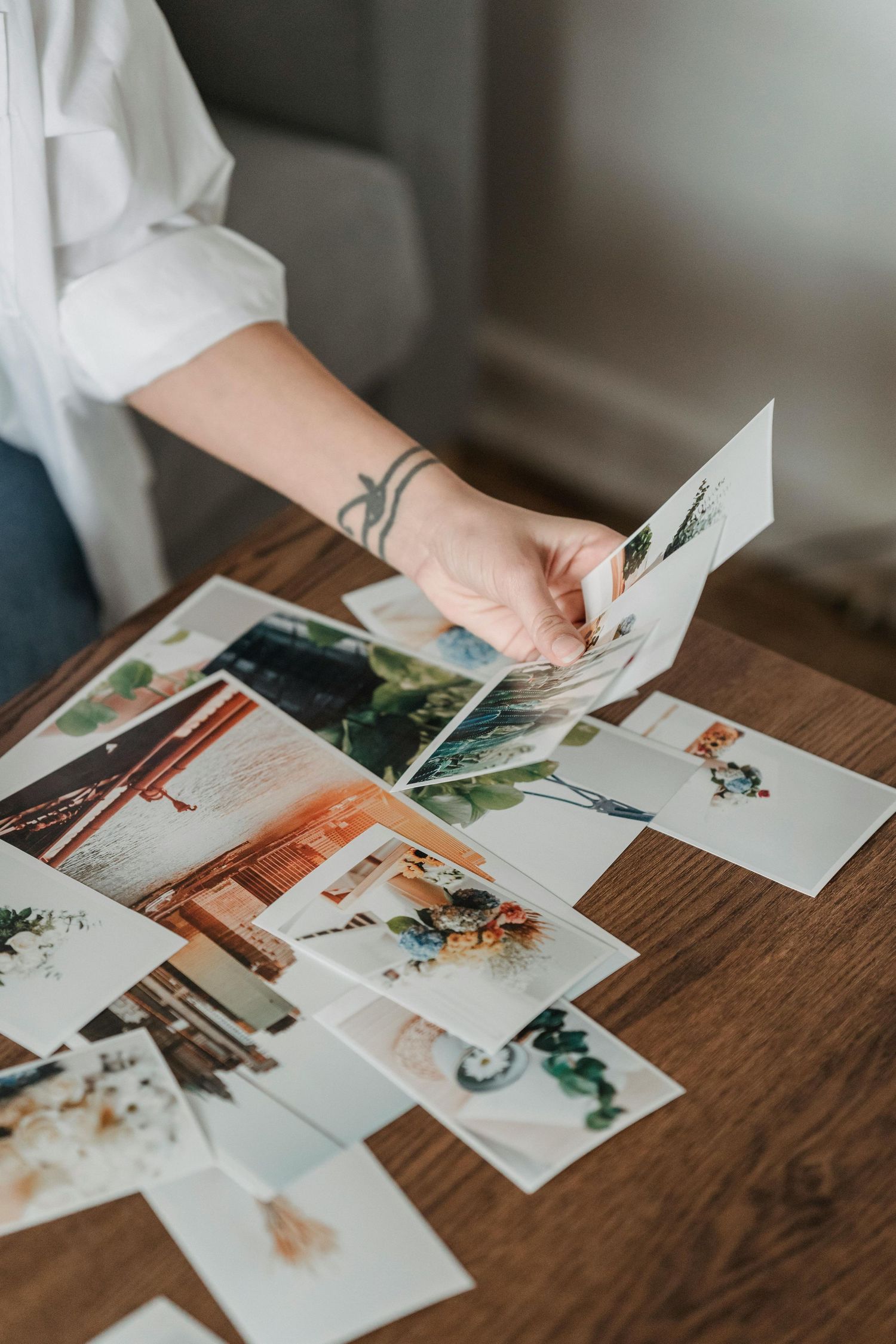 Person in white sleeve sorting through photographs on wooden desk.