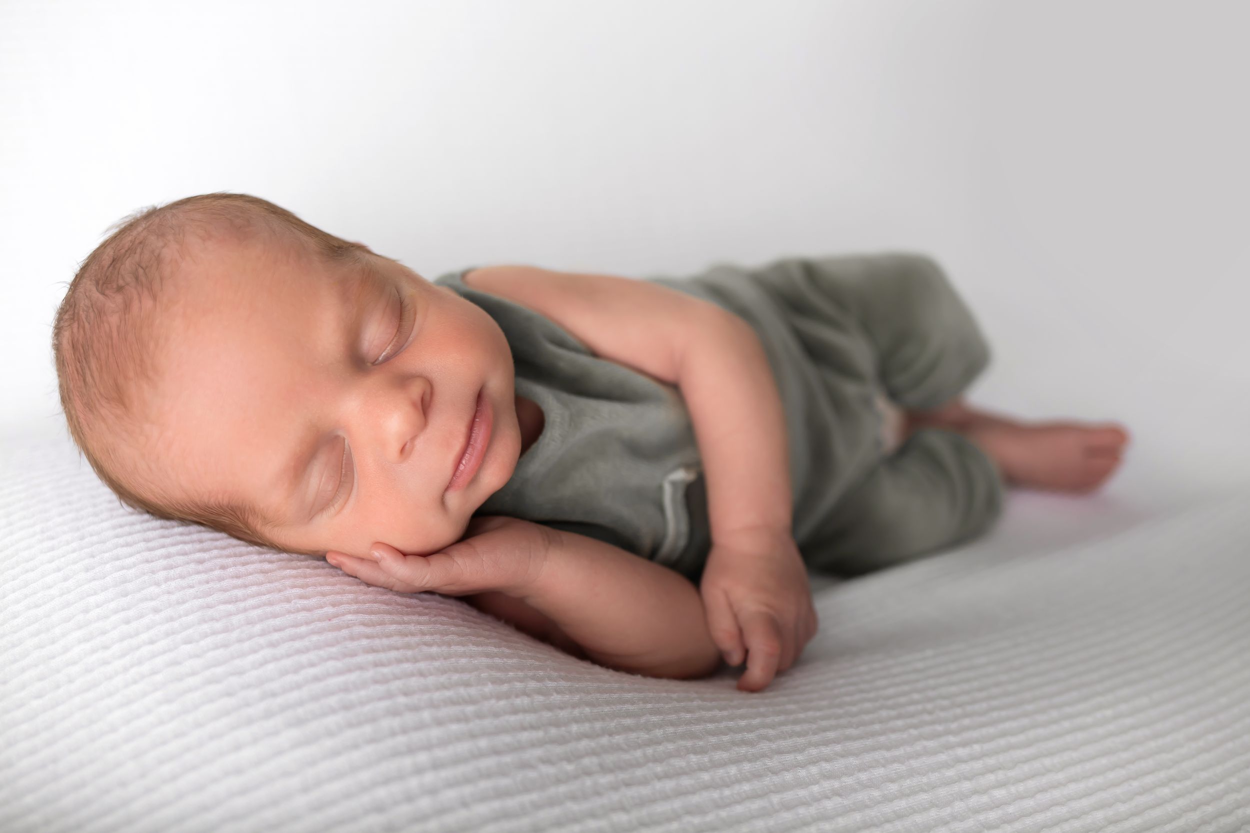 A peaceful newborn baby in gray outfit sleeping on white textured background.