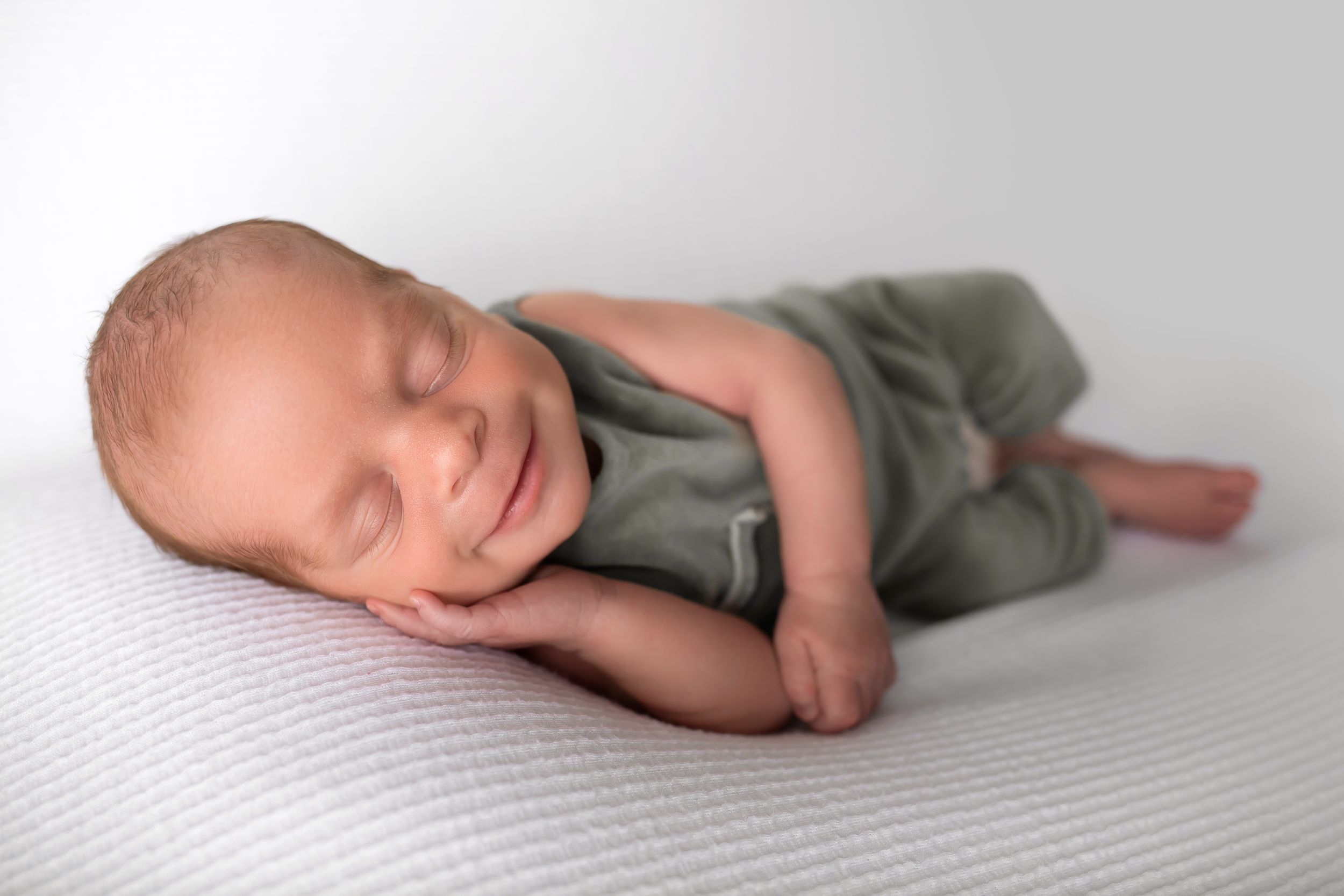 Sleeping newborn in gray outfit lying on white textured surface in studio setting.