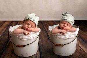 Twin babies sleeping in matching buckets wearing personalized beanies.