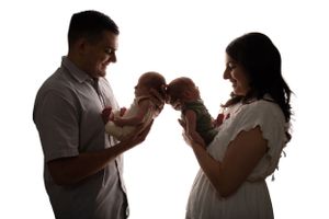 A silhouetted couple holds their newborn baby against a white background.
