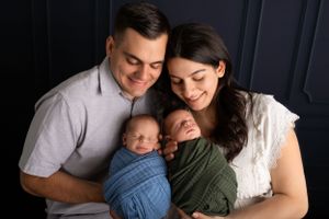 Parents snuggle with their twin newborns wrapped in blue and green swaddles.