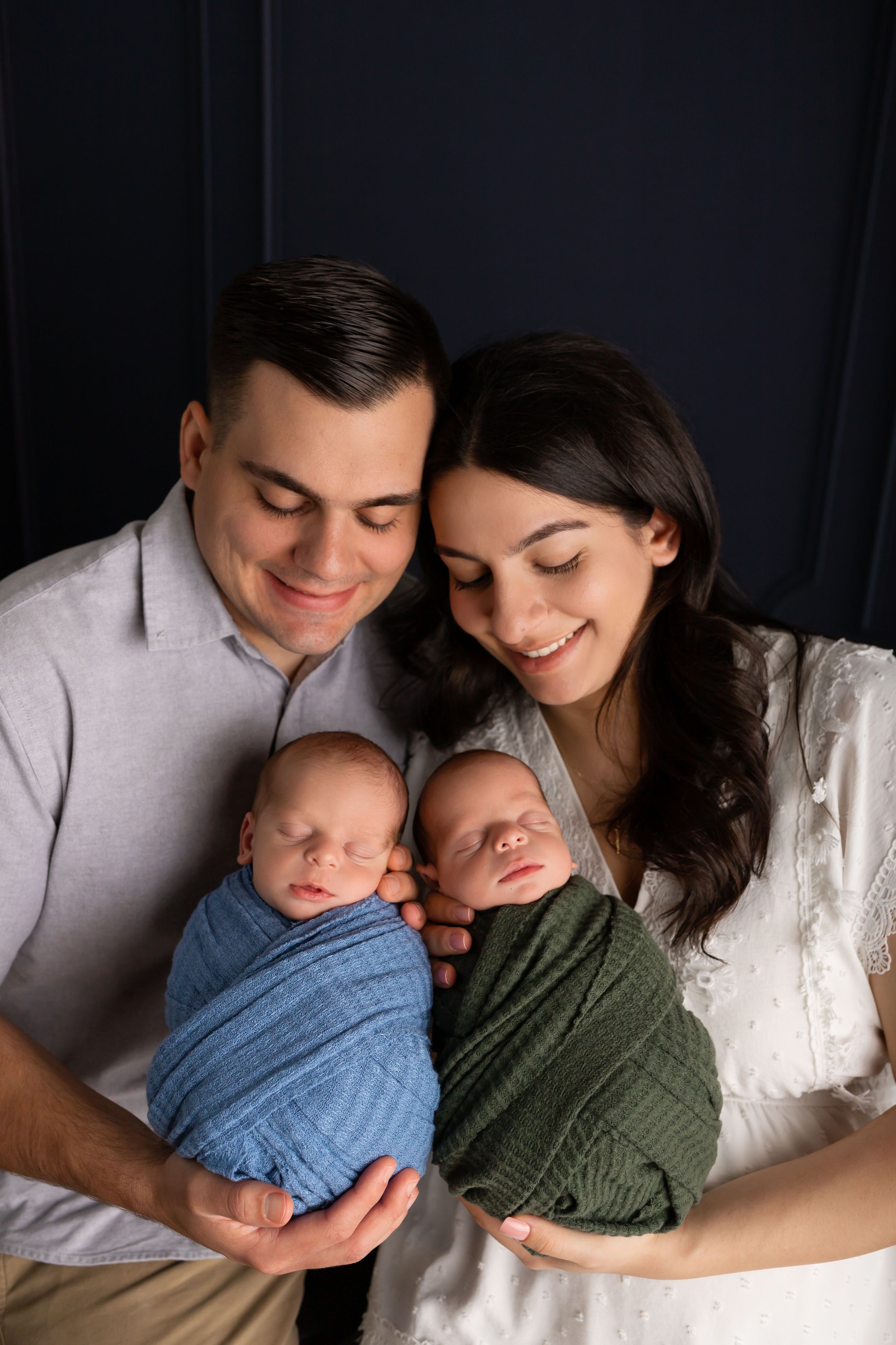 Parents gazing lovingly at their twin newborns wrapped in blue and green swaddles.