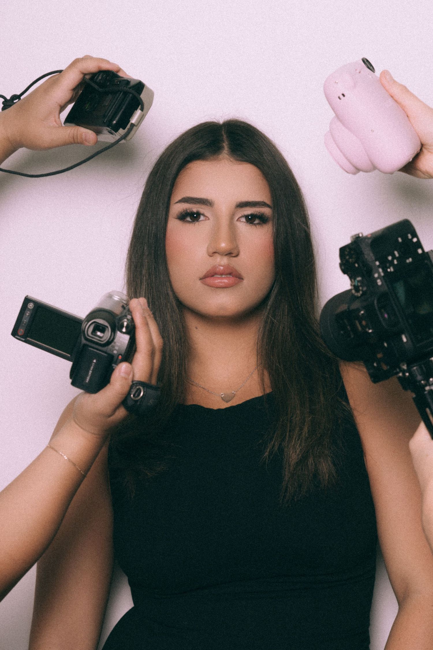 Artistic triptych photo series showing a model in black holding vintage cameras against a pink background.