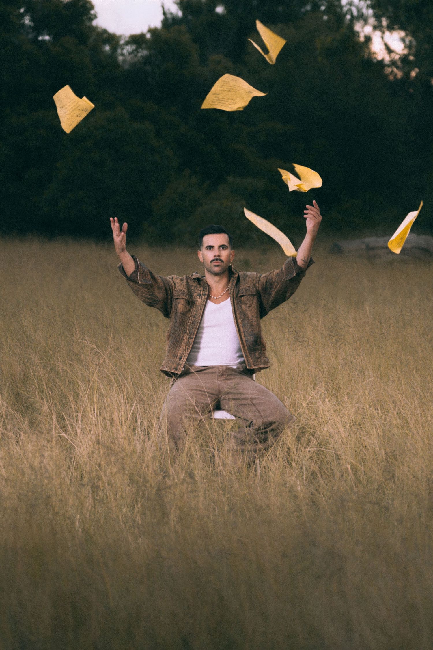 A person sitting in tall grass throws yellow paper airplanes into the air in a sequence of action shots.