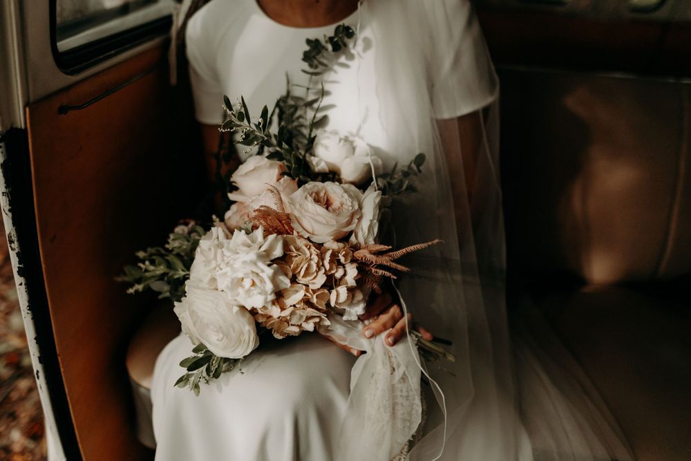 A delicate white and blush wedding bouquet held in a classic Volkswagen bus.