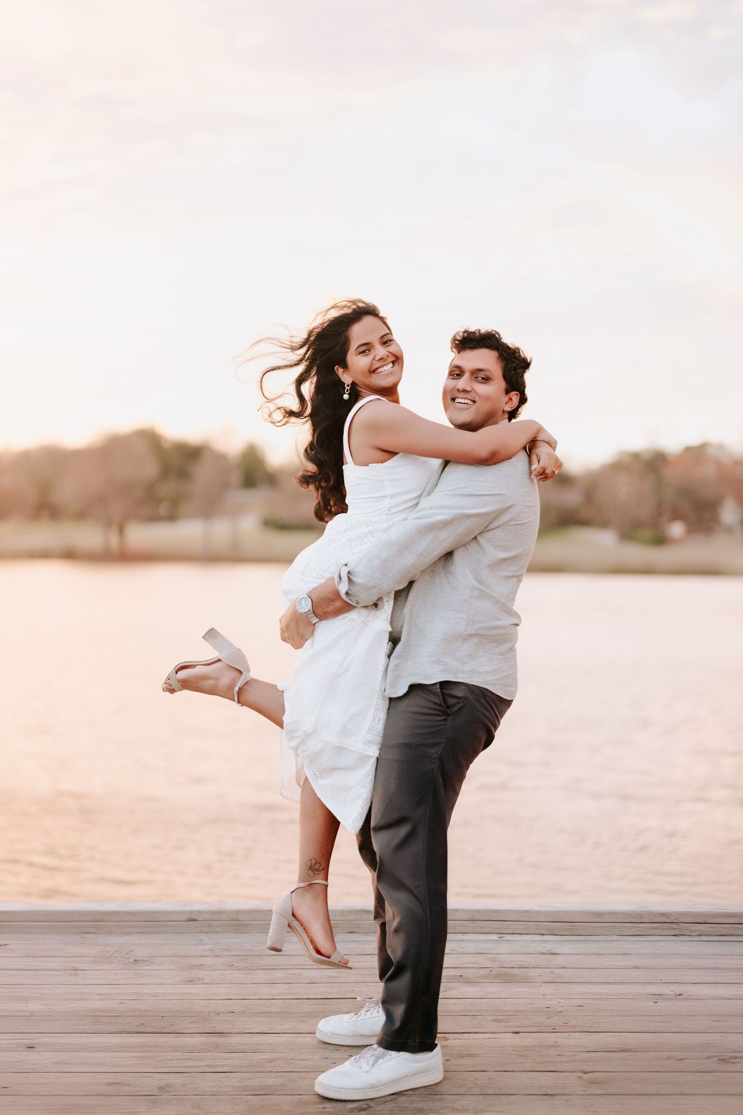A couple dances playfully on a wooden dock at sunset, creating romantic silhouettes against the water.