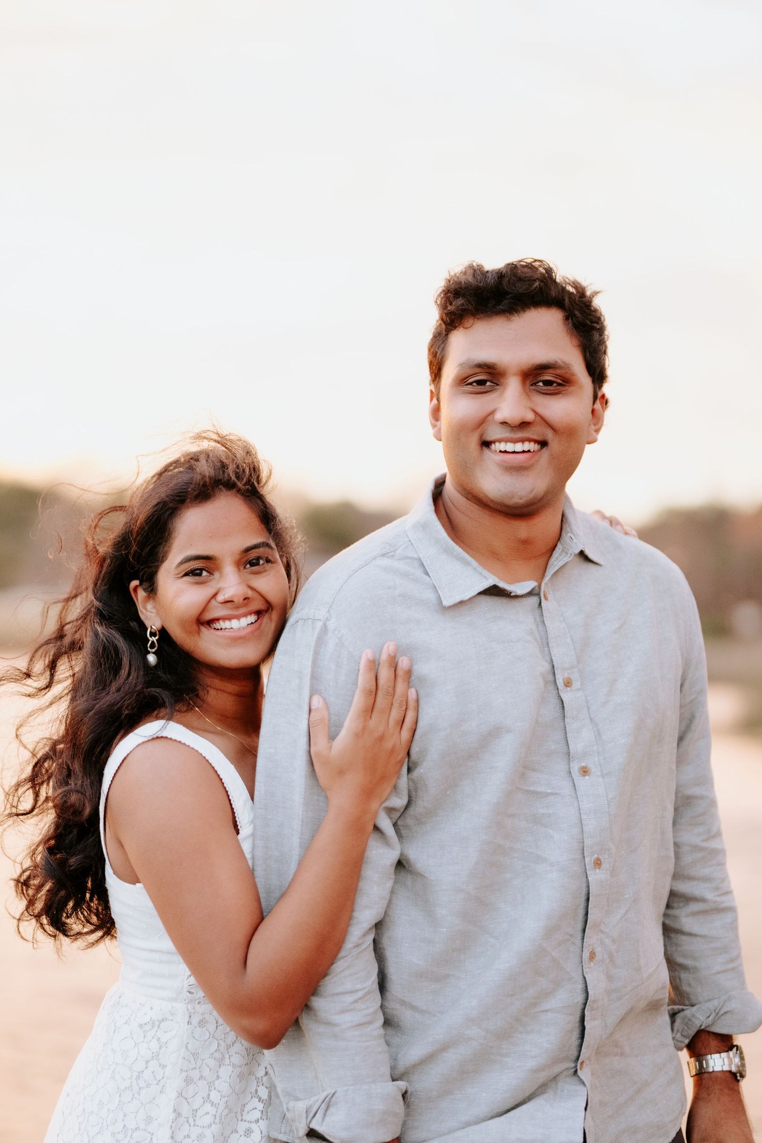 A couple embraces and smiles together during a romantic outdoor photoshoot at sunset.