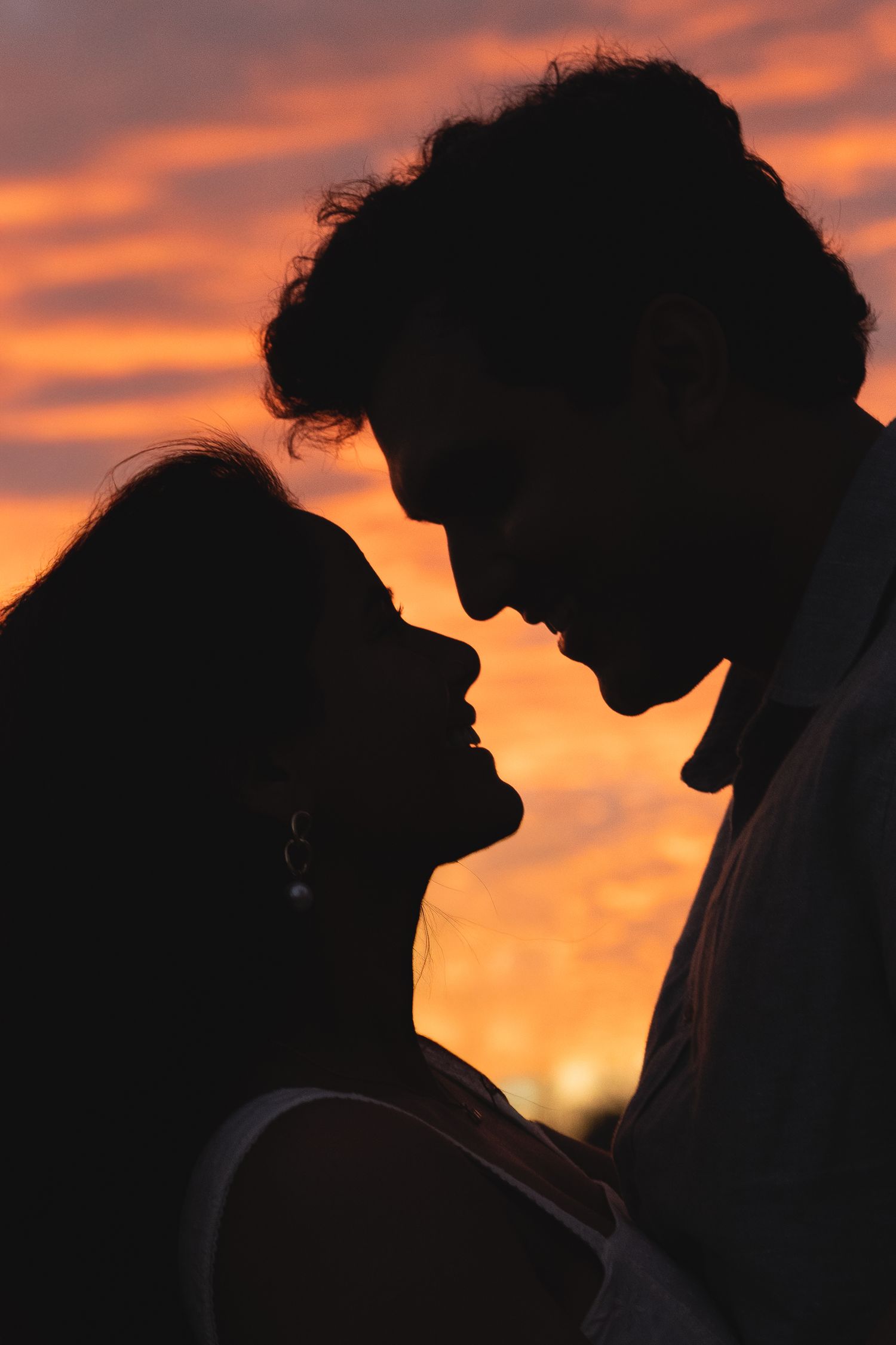 Silhouette of a romantic couple in close embrace against vibrant orange sunset sky.