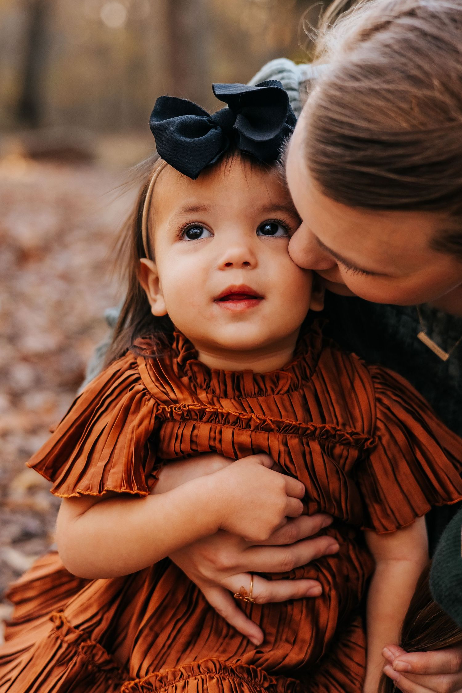 A tender moment between parent and child wearing a ruffled orange dress with black bow.