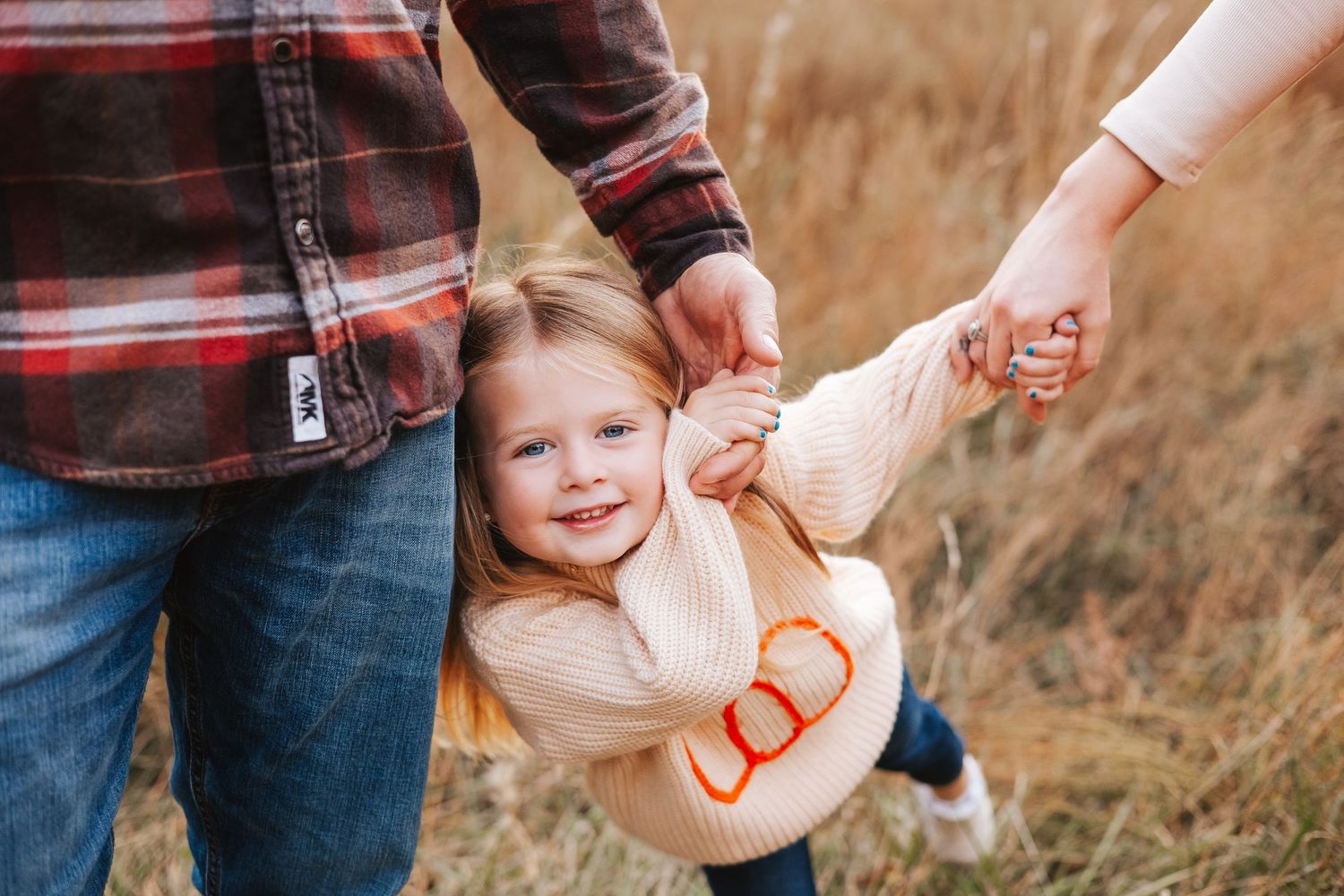 A playful family moment in a field as parents swing their child between them.