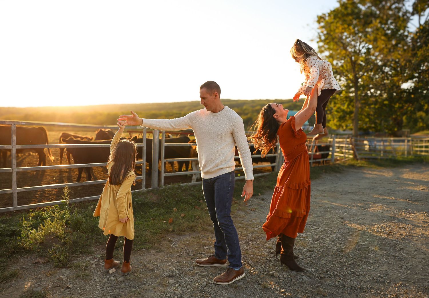 Family lying on a white blanket in a grassy field during golden hour sunset.