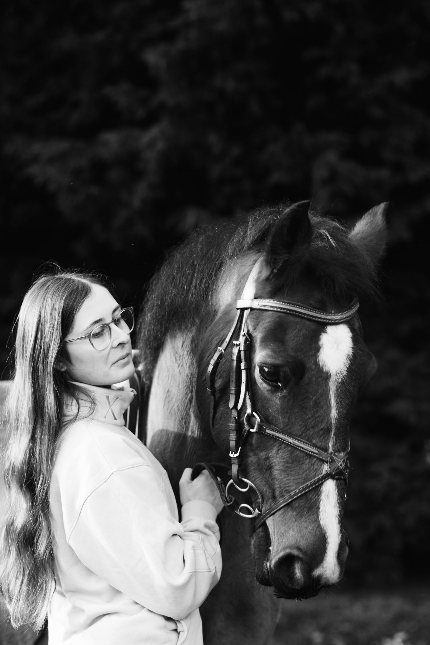 Black and white photo of someone bonding with a bay horse outdoors.